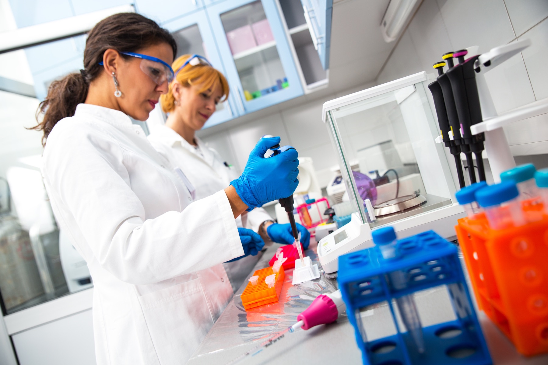 Researchers working with pipettes and sample racks at a laboratory bench.